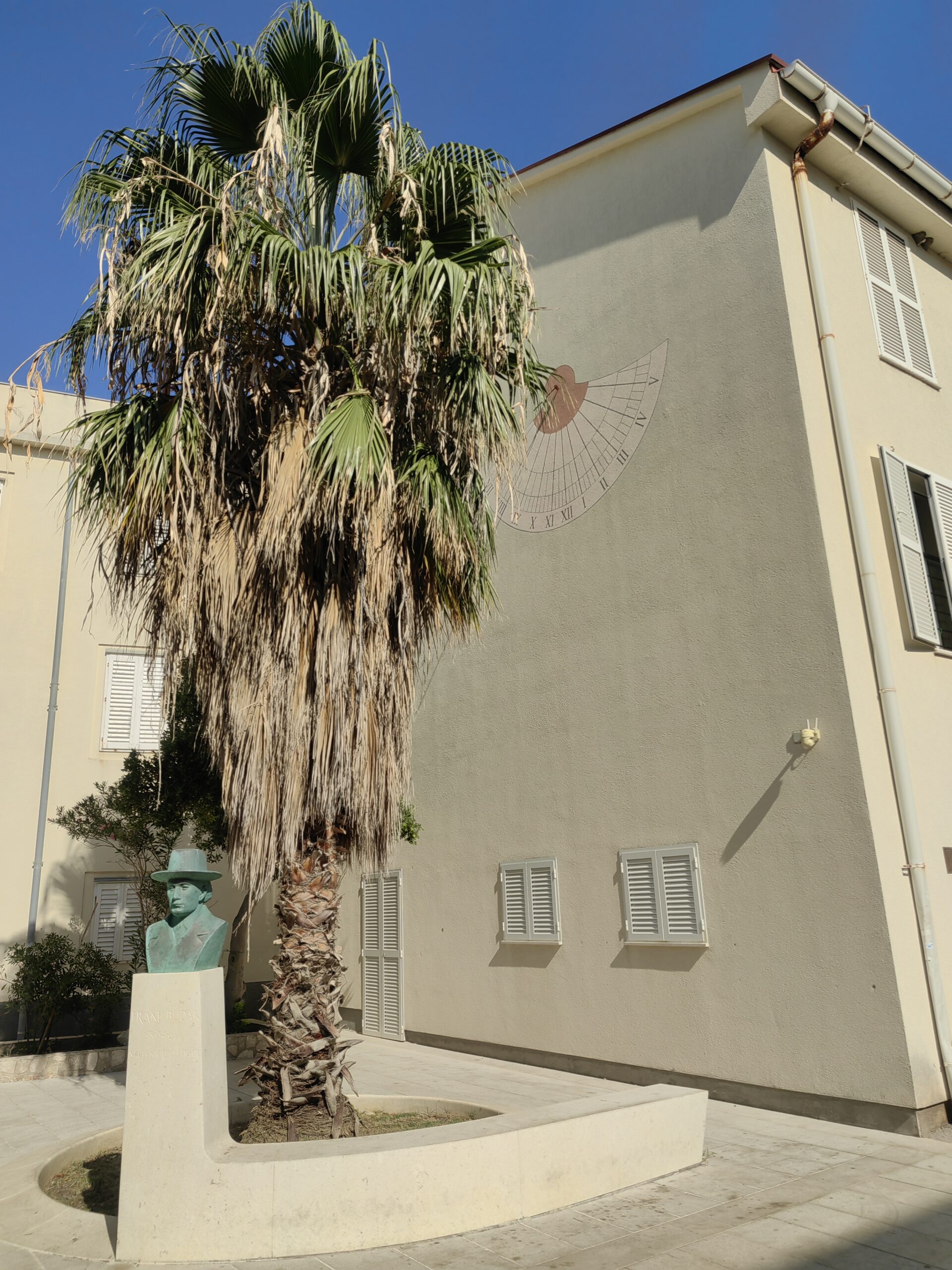 Sundial on a building beside a palm tree in the historic centre of Pag, Croatia
